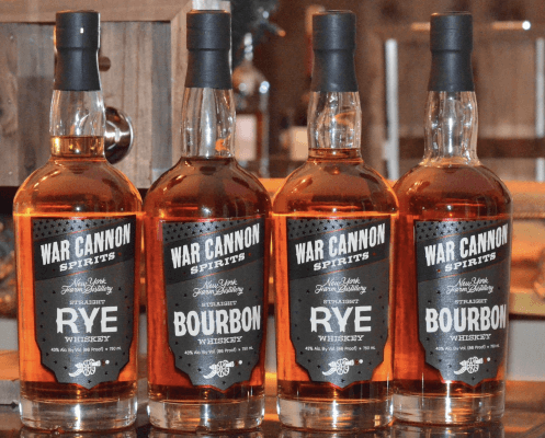 Four bottles of War Cannon Spirits whiskey are lined up, with two labeled as rye and two as bourbon, all featuring black and silver labels reminiscent of the elegance found at the Met Cloisters.